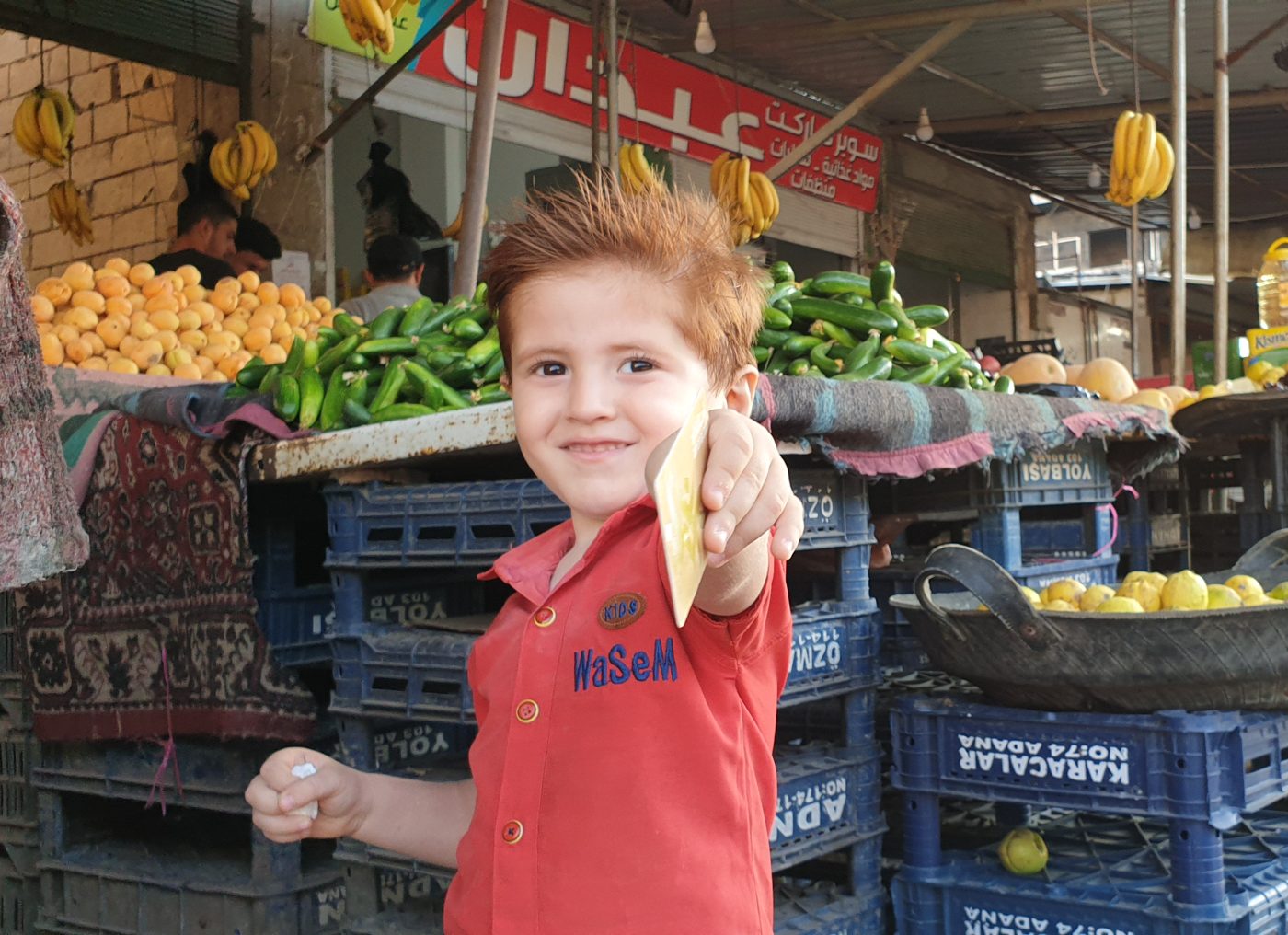 A boy at a produce market stall holds up his Amanacard